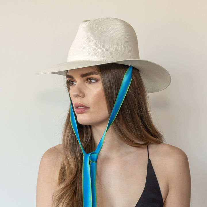 Khia Tullae The Amani white toquilla straw wide-brim hat with blue and green drop-down silk ribbon tied under chin, side view on model