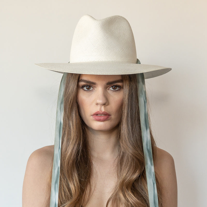 Khia Tullae The Bexley white toquilla straw wide-brim hat with blue and grey drop-down silk ribbon ties, front view on model