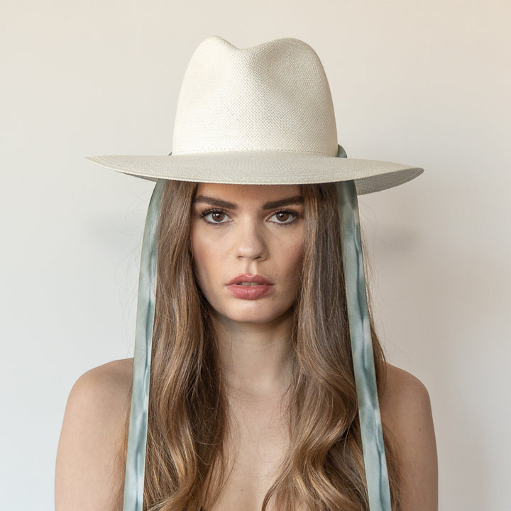 Khia Tullae The Bexley white toquilla straw wide-brim hat with blue and grey drop-down silk ribbon ties, front view on model