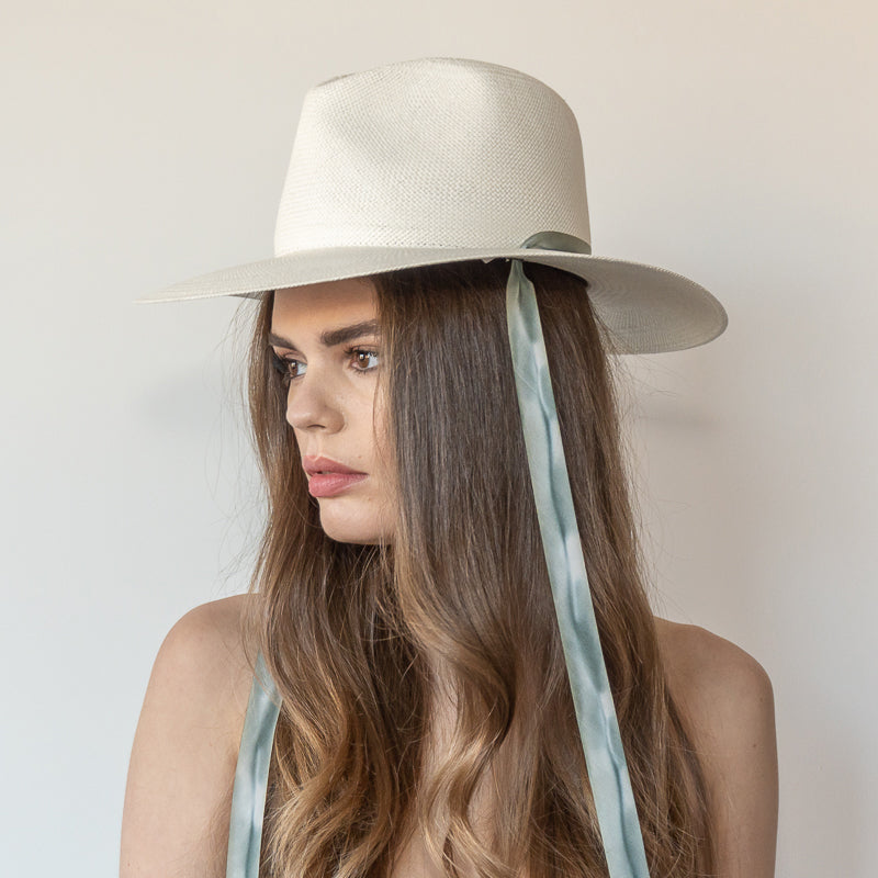 Khia Tullae The Bexley white toquilla straw wide-brim hat with blue and grey drop-down silk ribbon ties, side view on model