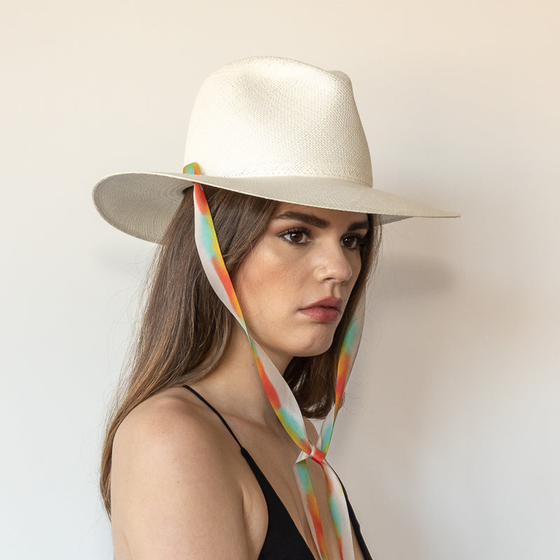 Khia Tullae The Billie white toquilla straw wide-brim hat with multicolor pastel rainbow drop-down silk ribbon tied under chin, side view on model