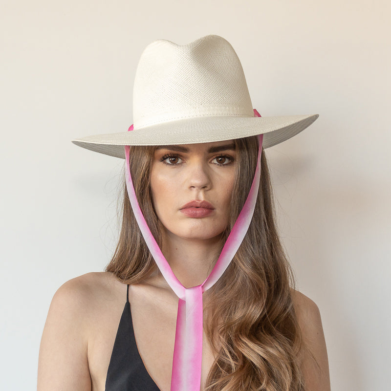 Khia Tullae The Brynn white toquilla straw wide-brim hat with pink and white drop-down silk ribbon tied under chin, front view on model