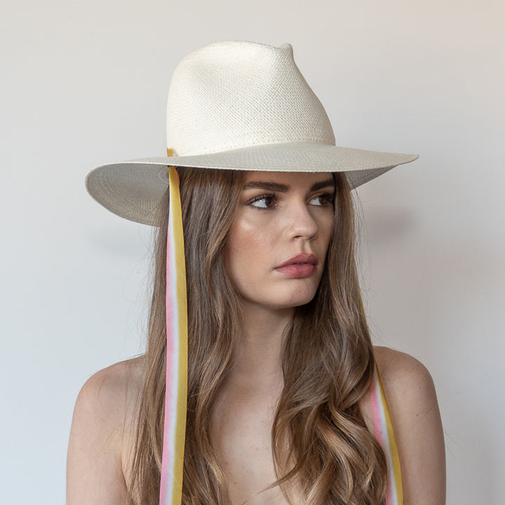 Khia Tullae The Margaux white toquilla straw wide-brim hat with golden caramel and pastel pink drop-down silk ribbon ties, side view on model