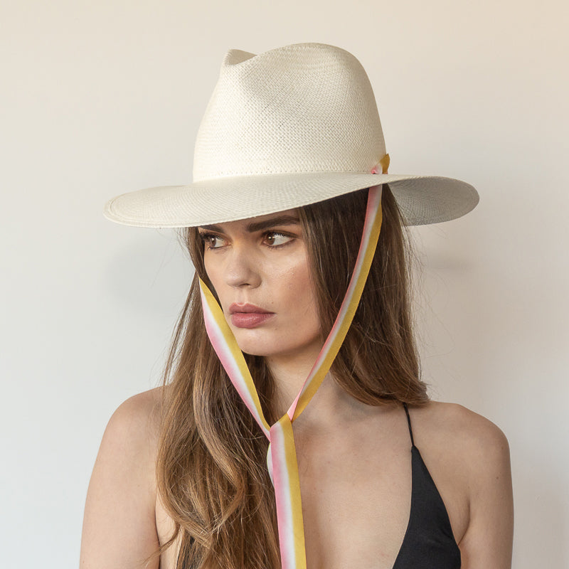 Khia Tullae The Margaux white toquilla straw wide-brim hat with golden caramel and pastel pink drop-down silk ribbon tied under chin, side view on model