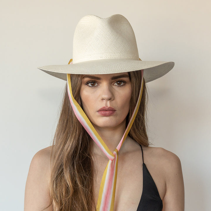 Khia Tullae The Margaux white toquilla straw wide-brim hat with golden caramel and pastel pink drop-down silk ribbon tied under chin, front view on model