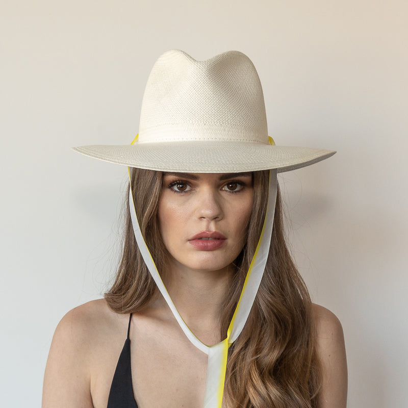 Khia Tullae The Siena white toquilla straw wide-brim hat with yellow and white drop-down silk ribbon tied under chin, front view on model