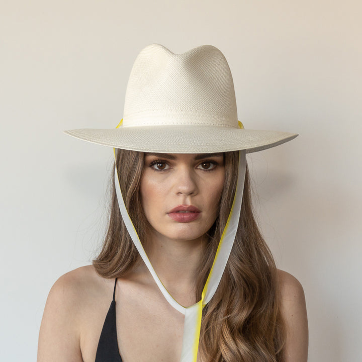 Khia Tullae The Siena white toquilla straw wide-brim hat with yellow and white drop-down silk ribbon tied under chin, front view on model
